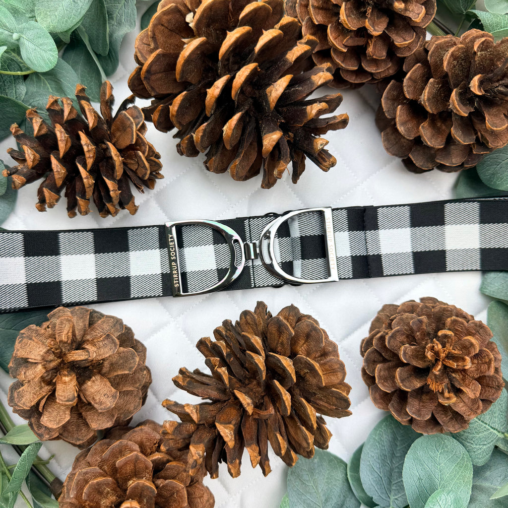 Black and grey plaid belt with pinecones and greenery on a white saddle pad