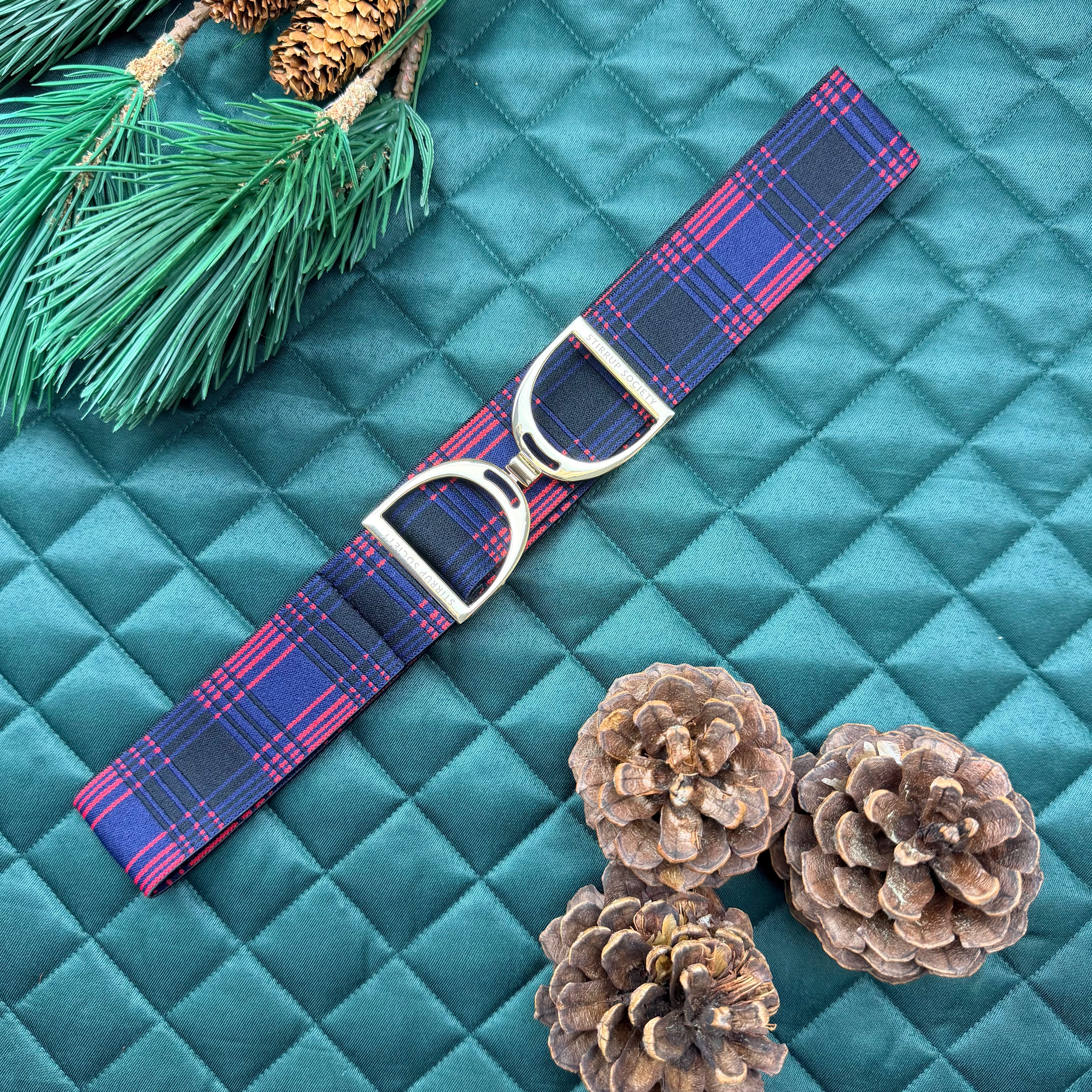 Blue and red plaid equestrian belt on a green saddle pad with pine cones and greenery.